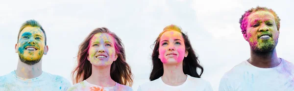 Panoramic shot of handsome african american man and cheerful friends with holi paints on faces — Stock Photo