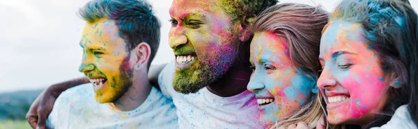 Panoramic shot of woman smiling near multicultural friends with holi paints on faces — Stock Photo