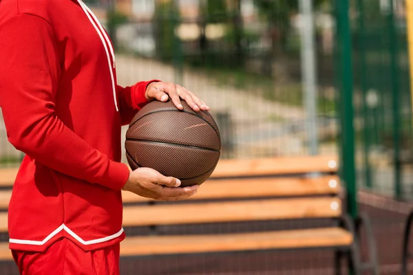Vista parcial del jugador de baloncesto sosteniendo la pelota cerca del banco de madera - foto de stock
