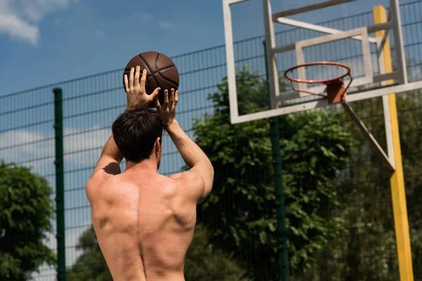 Visão traseira do jogador de basquete sem camisa jogando bola na cesta na quadra de basquete — Fotografia de Stock