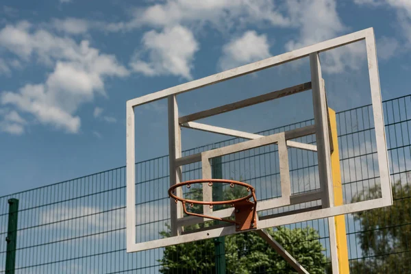 Aro de baloncesto en cancha de baloncesto bajo cielo azul nublado - foto de stock