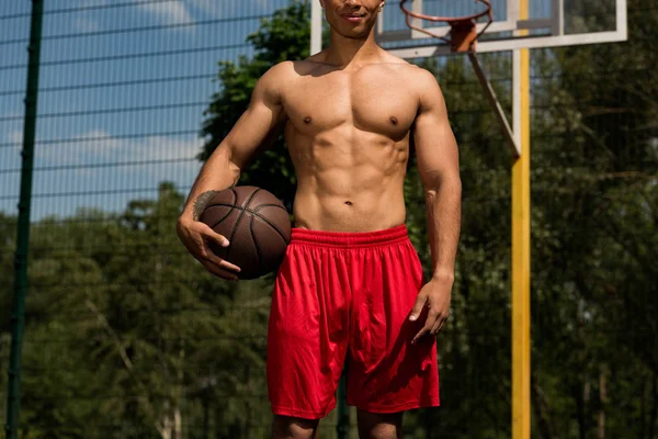 Частковий вигляд баскетболіста з м'ячем на баскетбольному майданчику в сонячний день — стокове фото