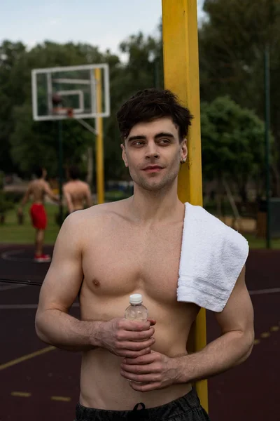 Sexy sportivo senza maglietta con asciugamano in possesso di bottiglia d'acqua al campo da basket — Foto stock