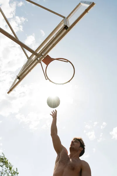 Вид снизу баскетболист без рубашки бросает мяч в корзину в солнечный день — стоковое фото
