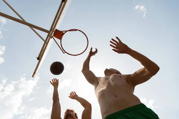 Vista dal basso dei giocatori di basket a torso nudo che lanciano palla nel cestino nella giornata di sole — Foto stock