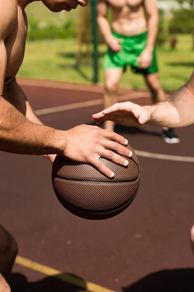 Vue partielle de sportifs torse nu jouant au basket sur le terrain de basket — Photo de stock