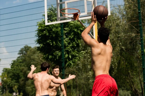 Спортсмены без рубашек играют в баскетбол на баскетбольной площадке в солнечный день — стоковое фото