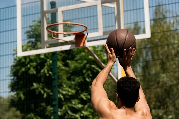 Vista trasera del jugador de baloncesto lanzando pelota en canasta en cancha de baloncesto - foto de stock