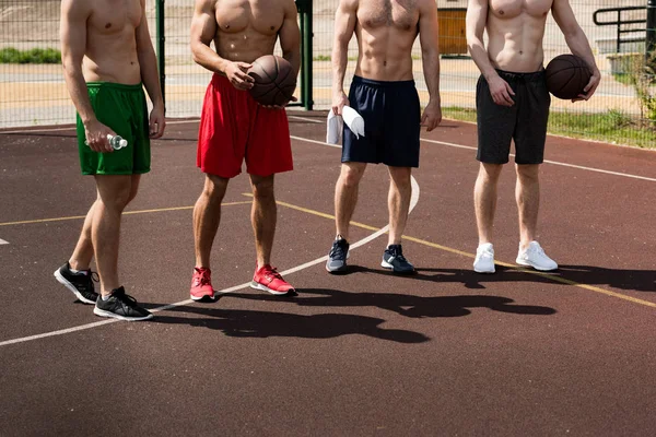 Vista cortada de quatro jogadores de basquete sem camisa com bolas na quadra de basquete — Fotografia de Stock