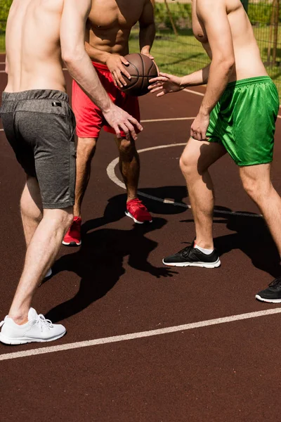 Cropped view of three shirtless sportsmen playing basketball at basketball court in sunny day — Stock Photo