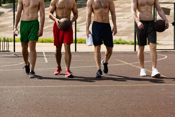 Vue recadrée de quatre joueurs de basket-ball torse nu avec des balles sur le terrain de basket — Photo de stock