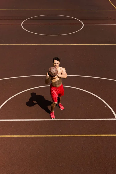 Vista aérea de sexy sin camisa jugador de baloncesto de carrera mixta con pelota en la cancha de baloncesto - foto de stock