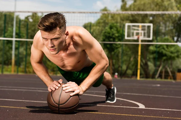 Sportif torse nu sexy faisant push ups avec balle au terrain de basket — Photo de stock