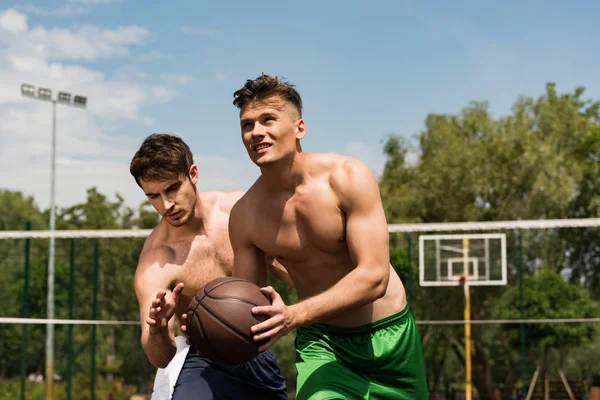 Sportivi muscolosi senza maglietta che giocano a basket al campo da basket sotto il cielo blu — Foto stock