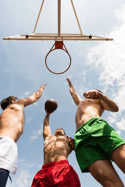 Vista inferior de deportistas sin camisa jugando baloncesto bajo el cielo azul - foto de stock