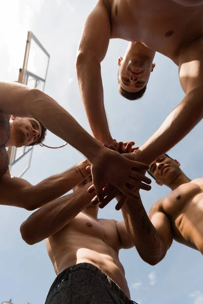 Vista dal basso di quattro sportivi a torso nudo che toccano le mani sotto il cielo nella giornata di sole — Foto stock