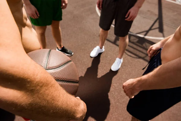Vista recortada de cuatro deportistas con pelota en cancha de baloncesto - foto de stock