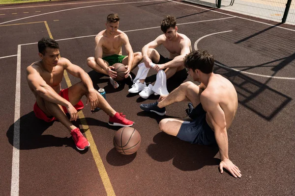 Чотири втомлені сорочки без баскетболісти сидять на баскетбольному майданчику в сонячний день — стокове фото