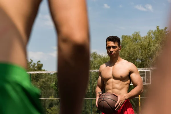 Cropped view of sexy shirtless sportsmen playing basketball under blue sky — Stock Photo
