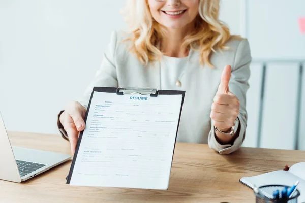 Cropped view of woman holding clipboard with resume lettering and showing thumb up — Stock Photo