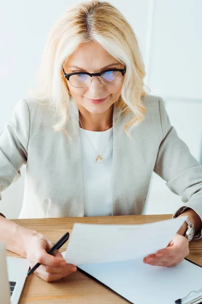 Вибірковий фокус жінки в окулярах тримає папір в офісі — стокове фото