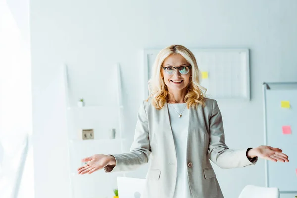 Fröhliche blonde Frau mit Brille gestikuliert im Büro — Stockfoto