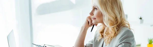 Plano panorámico de mujer rubia reflexiva sosteniendo pluma en la oficina — Stock Photo