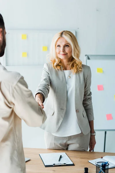 Selective focus of blonde recruiter shaking hands with employee in office — Stock Photo