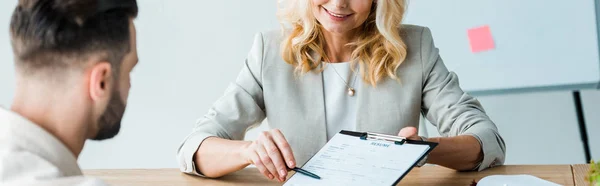 Panoramaaufnahme eines Personalvermittlers, der Stift in der Nähe des Klemmbretts hält und einen bärtigen Mann ansieht — Stockfoto