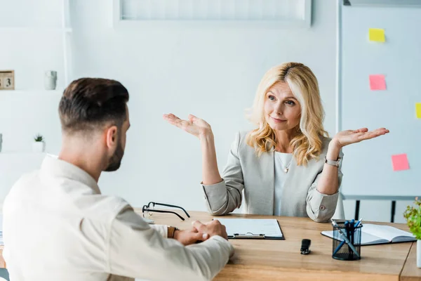 Selective focus of blonde recruiter gestruing and looking at bearded man — Stock Photo