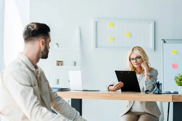 Selective focus of recruiter looking at clipboard near bearded man — Stock Photo