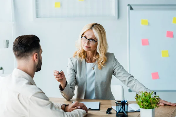 Selektiver Fokus attraktiver blonder Personalvermittler mit Stift und Blick auf bärtigen Mann — Stockfoto