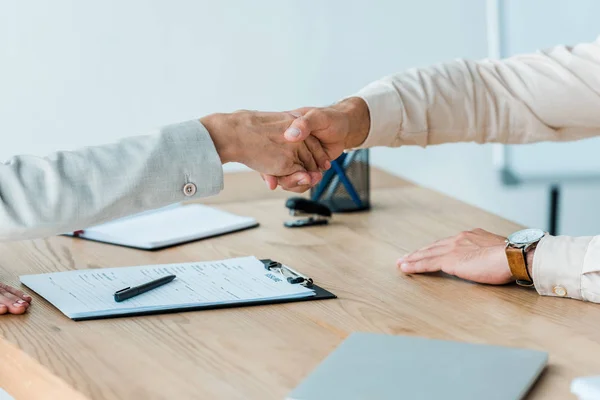 Vista recortada del hombre y la mujer estrechando las manos cerca de la mesa - foto de stock