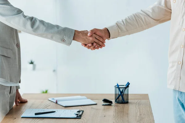 Vista recortada del hombre y reclutador estrechando las manos cerca de la mesa - foto de stock