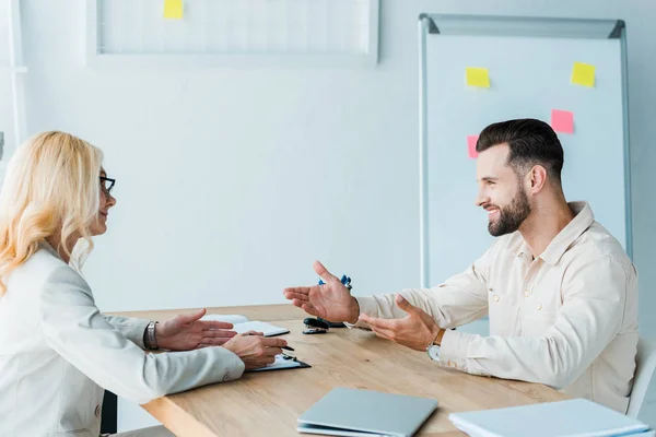 Fröhlicher bärtiger Mitarbeiter gestikuliert in der Nähe attraktiver Personalvermittler — Stockfoto