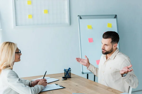 Empregado barbudo alegre mostrando gesto encolher de ombros perto recrutador atraente — Stock Photo