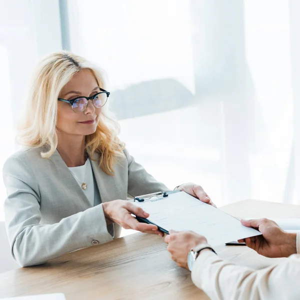 Selektiver Fokus des blonden Recruiters, der Klemmbrett und Stift in der Hand hält und neben dem Mitarbeiter sitzt — Stockfoto