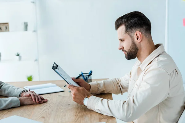 Cropped view of recruiter near handsome bearded man looking at clipboard — Stock Photo