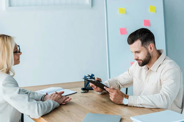 Selektiver Fokus eines gutaussehenden bärtigen Mannes, der auf Klemmbrett schaut — Stockfoto