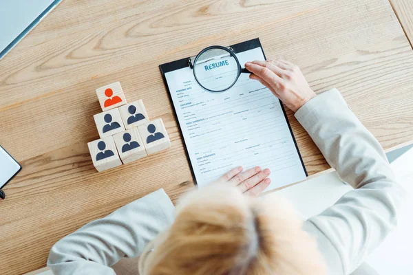Selective focus of blonde recruiter holding magnifier near clipboard — Stock Photo
