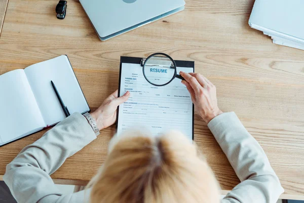 Selective focus of blonde woman holding magnifier near clipboard — Stock Photo