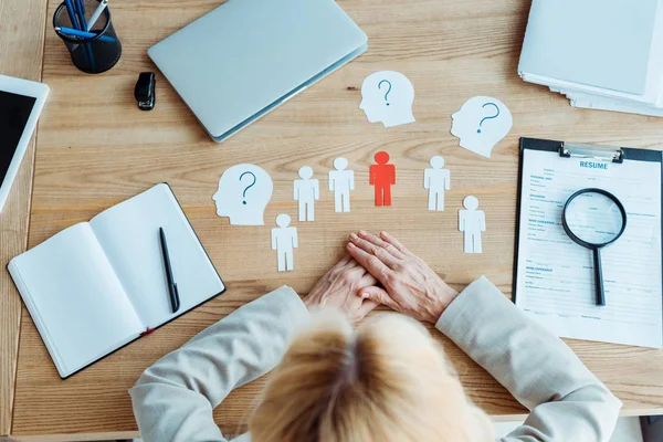 Vista superior da mulher com as mãos apertadas perto de formas de papel e notebook em branco na mesa — Fotografia de Stock