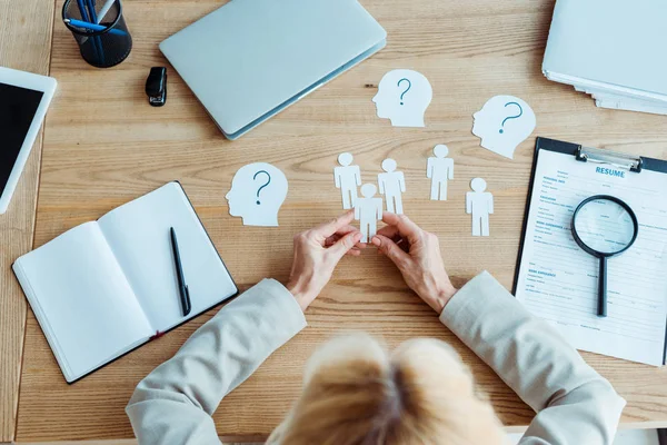 Cropped view of woman holding paper human shapes near table — Stock Photo