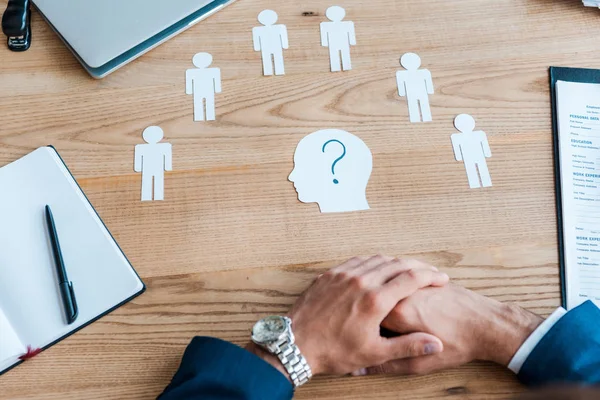 Cropped view of recruiter with clenched hands near paper human shapes on table — Stock Photo