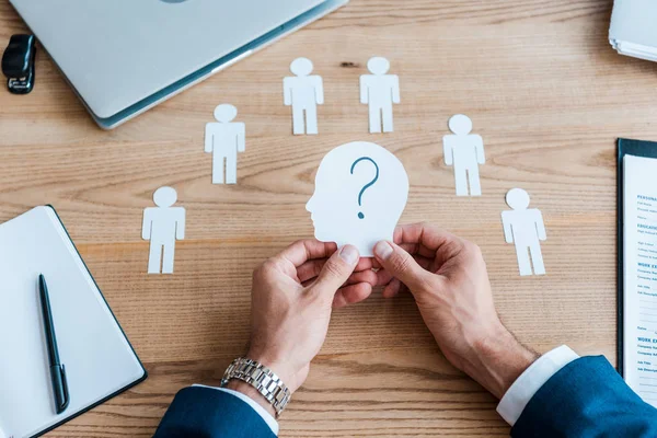 Vista recortada del reclutador sosteniendo papel forma humana con signo de interrogación en la mesa - foto de stock
