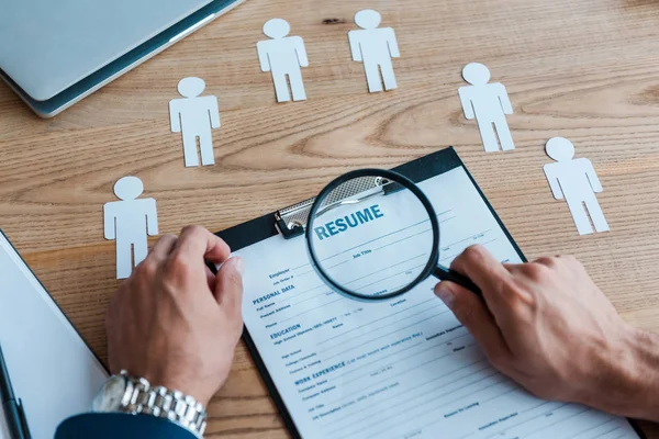 Vista recortada del hombre sosteniendo lupa cerca del portapapeles con curriculum vitae - foto de stock