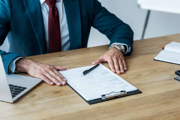 Ausgeschnittene Ansicht eines Recruiters, der neben Laptop und Klemmbrett auf einem Holztisch sitzt — Stockfoto