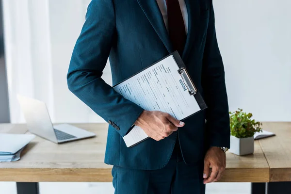 Vista recortada del hombre de pie y sujetando el portapapeles con letras de curriculum vitae - foto de stock