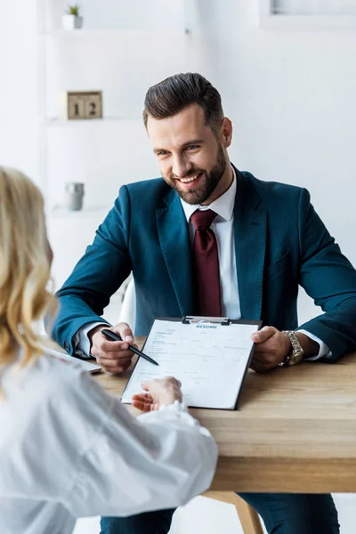 Selective focus of happy recruiter holding pen near clipboard and looking at blonde employee — Stock Photo