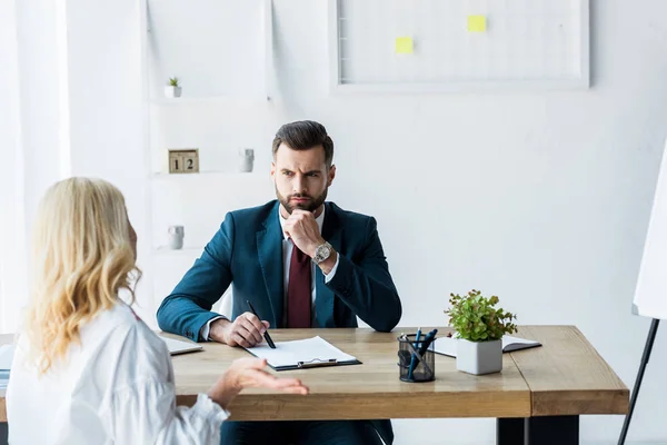 Selective focus of thoughtful recruiter in suit looking at blonde employee showing shrug gesture — Stock Photo